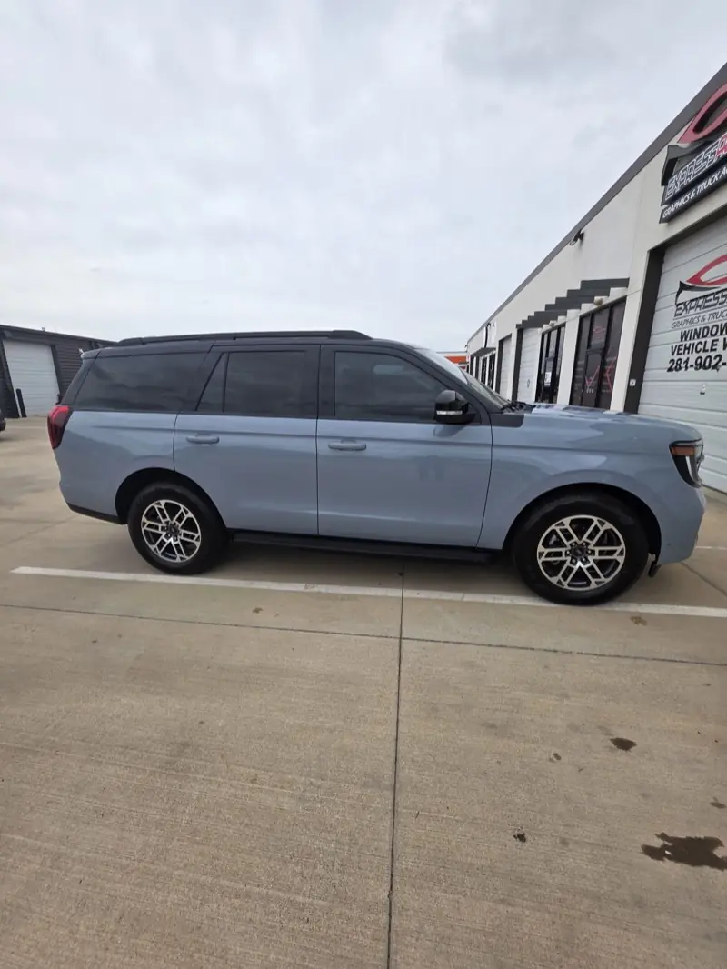 Light blue full-size SUV with freshly tinted windows, parked at ExpressAutoTNT in Katy, TX