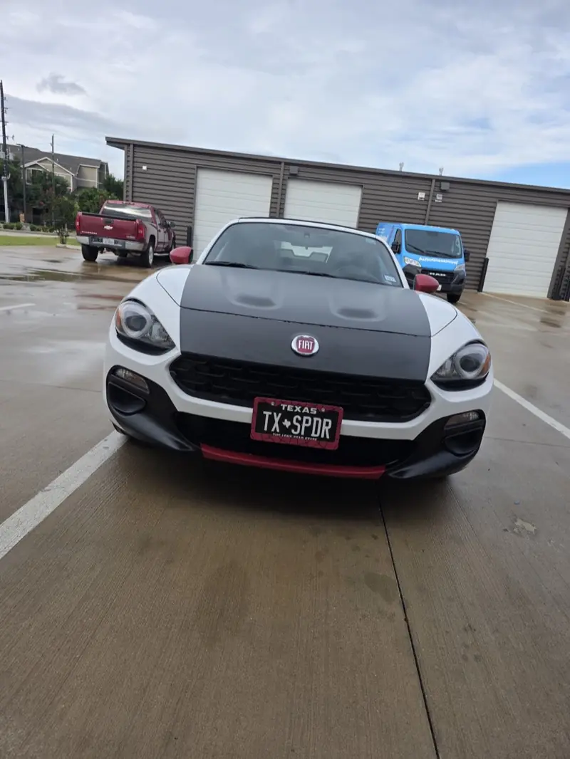 Front of a white convertible sports car with a matte black hood wrap, at ExpressAutoTNT in Katy, TX